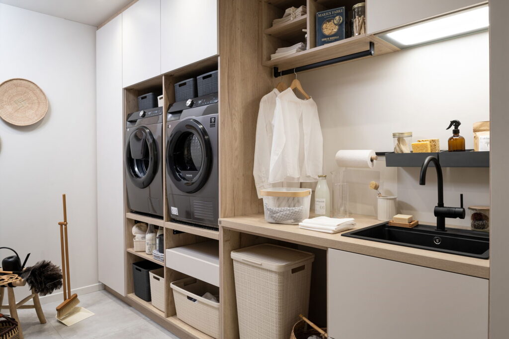 Waschküche im Keller mit erhöht eingebauter Waschmaschine und Trockner, offenen Regalen, Stauraum und Arbeitsfläche